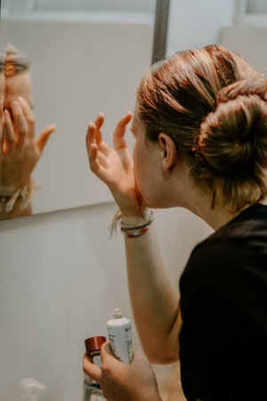 A vertical closeup shot of a female putting on face cream in a bathroom mirror