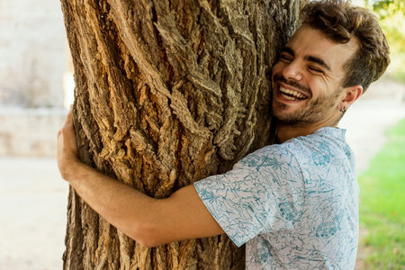 A happy Spanish guy hugging a tree in a park with a lovely smileの写真素材