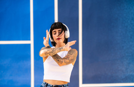 A young attractive caucasian female with tattoos listening to music with headphones and dancing