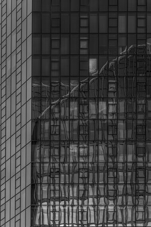 A vertical grayscale shot of a tall glass skyscraper with reflections in the windowsの写真素材