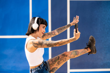 A young attractive caucasian female with tattoos listening to music with headphones and taking...