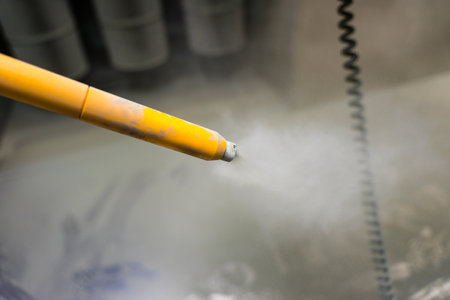 Horizontal shot of a tip of the powder coating gun with visible air filters and a ground wire in the...