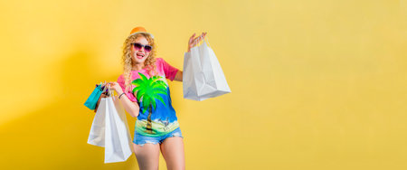 Happy young girl in bright casual clothes, in hat and sunglasses stands on yellow background. In...