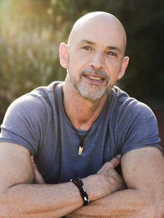 A portrait of a handsome bald middle-aged man in a gray t-shirt outdoors in sunlight