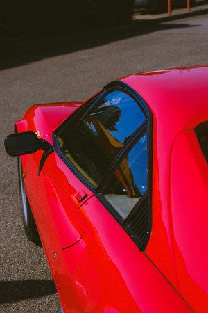A vertical shot of a shiny red sports car parked outdoors on a sunny dayの写真素材