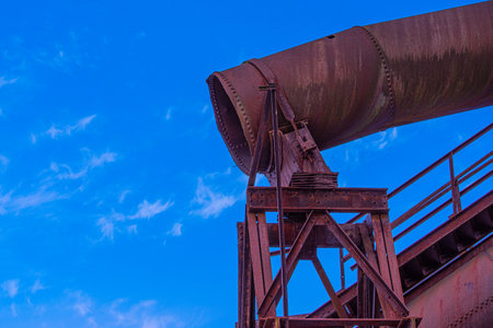 An eerie view of the rusty gas tube on a metallic structure on a clear blue sky