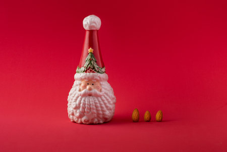 A closeup of a Santa Claus Christmas ornament with almonds against a red background