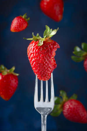 A vertical shot of a strawberry on a for against a blue blurry backgroundの写真素材