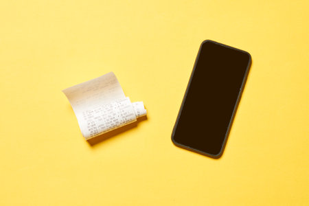 A cash register receipt and a black smartphone isolated on yellow background