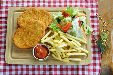A top view of adelicious breakfast of french fries, fried fish patties, salad, and sauce on the...