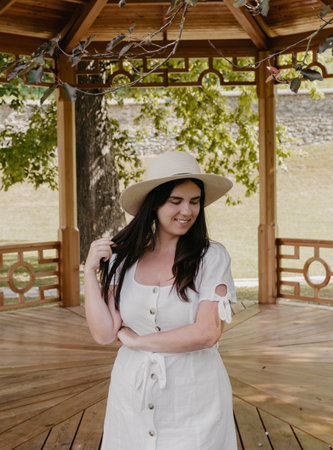 Lifestyle portrait of beautiful young woman smiling, standing in front of wooden pavilion in park.の写真素材