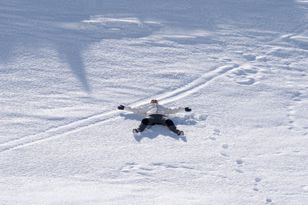 A view of a caucasian woman dressed in a skiing suit and lying in the snow on the mountainの写真素材