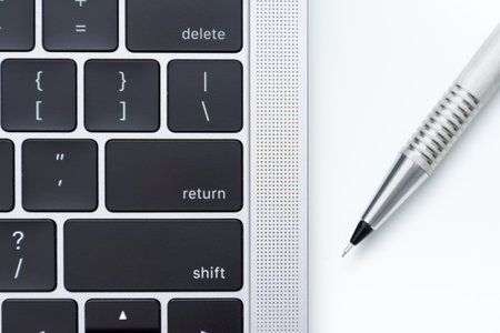 A closeup shot of a laptop keyboard and a pen