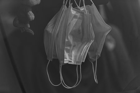 A grayscale shot of used surgical masks hanging in the roomの写真素材