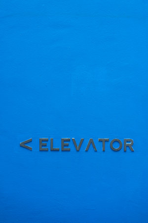 Sign on blue wall indicating the direction to the elevator . Vertical shotの写真素材