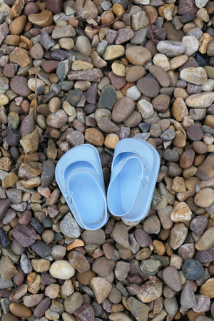 A top-view of blue plastic child's shoes on the beach pebblesの写真素材