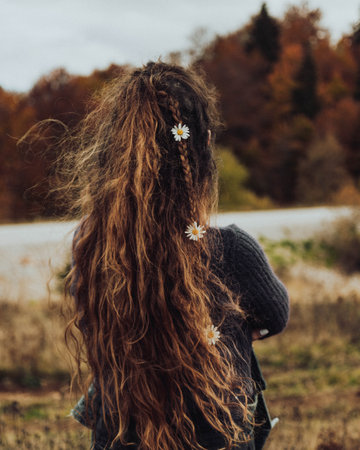 A vertical shot of a woman with long curly hair and daisies in her hair