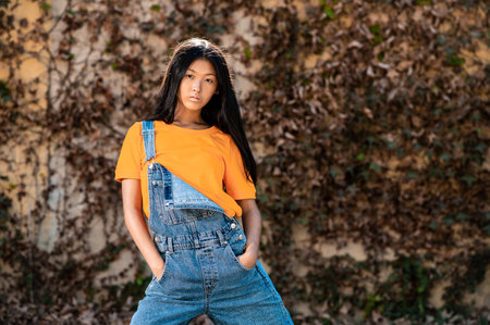 A pretty East Asian lady with dark hair and jeans overalls posing while demonstrating dance movesの写真素材