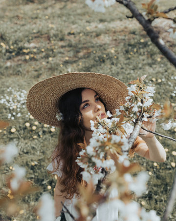 A young Bosnian woman in a hat posing in the beautiful cherry blossom gardenの写真素材
