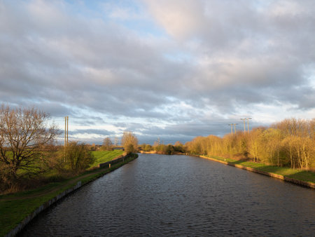 A vanishing point shot of a river between grassy fields under a gloomy cloudscape during sunsetの写真素材