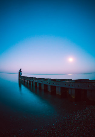 A scenic view of a man standing on the edge of a dock at dusk