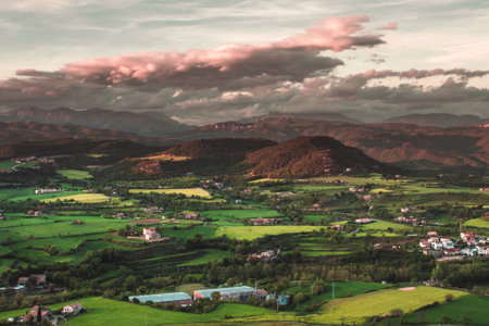The beautiful scenery of a village on green fields with mountains background during sunsetの写真素材