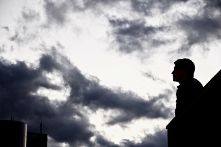 A silhouette of a mysterious male sitting against the cloudy rainy sky