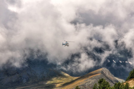 A helicopter flying above hills covered in the snow on a sunny day in the countrysideの写真素材