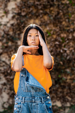 A pretty East Asian lady with dark hair and jeans overalls posing while demonstrating dance moves