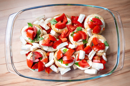 The appetizing salad with tomatoes, mushrooms, greens and cheese in a transparent dish on the tableの写真素材