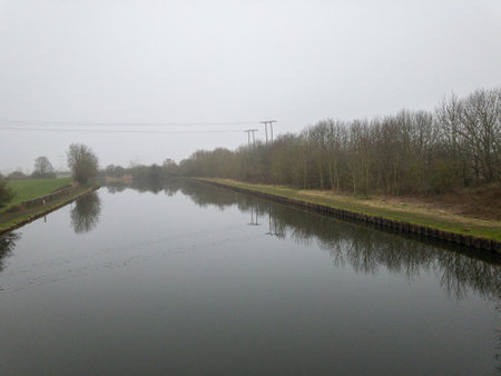 A vanishing point shot of a river between grassy fields under a foggy skyの写真素材