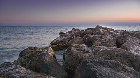 A beautiful horizon of the sea and the rocks on the beach on a sunsetの写真素材