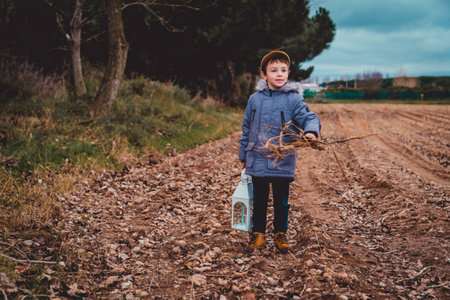 A boy in a blue coat is holding a lantern and a bunch of wood.の写真素材