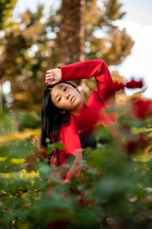 A portrait of an elegant East Asian woman wearing a red suit and posing in a garden in autumn in...