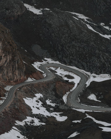 A vertical shot of an empty street in the mountains covered with some snow