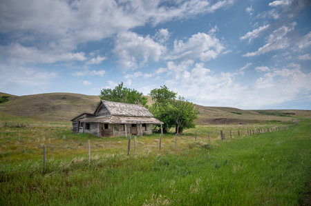 A horizontal shot of a destroyed wooden home on a sunny green field under a cloudy sky on the horizonの写真素材