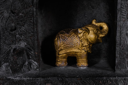 A small golden Indian elephant statue positioned in a dark black wallの写真素材