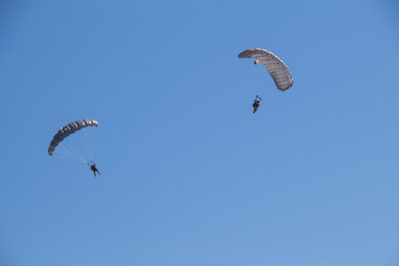 The two adventurous people flying in the bright blue sky with parachutes