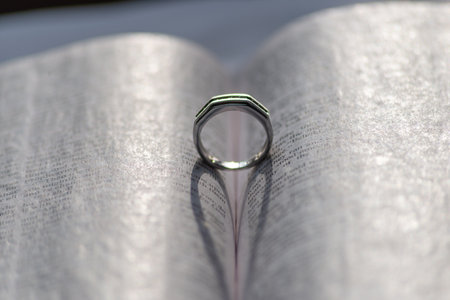 A silver ring between the pages of a book forming a heart shape with its shadow in the sunの写真素材