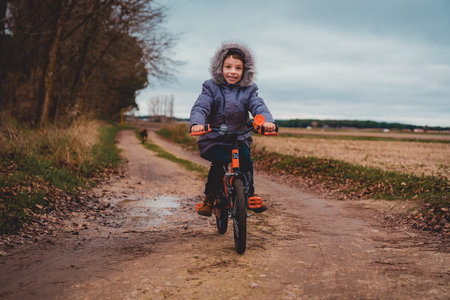 A boy in a blue coat is riding a bicycle on the rural road.