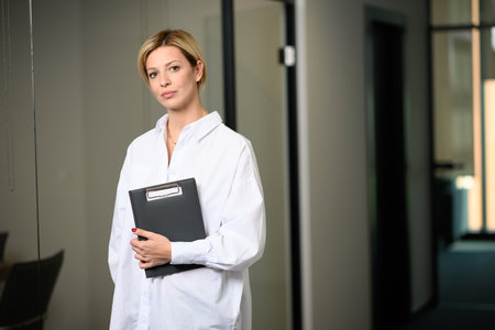 A horizontal shot of a short hair blonde businesswoman folder in hand in the office