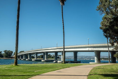 A long curved concrete bridge over a river under a clear blue skyの写真素材