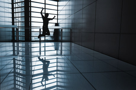 A shot of a silhouette of a man jumping in happiness in a building interior with tile ground and wallsの写真素材