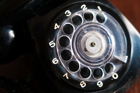 A macro shot of a black vintage dial telephone on a wooden surface