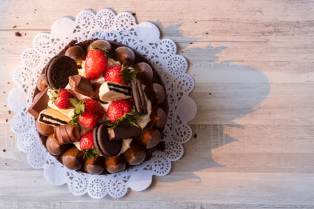 A top view shot of a cake with strawberries, chocolate balls, and cookies at the top on a wooden...