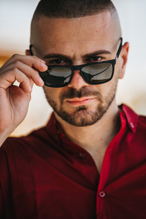 A cool handsome Caucasian man wearing an elegant red shirt and sunglasses posing outdoorの写真素材