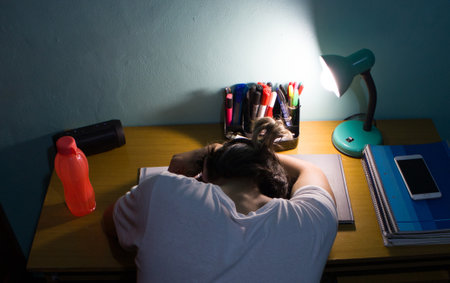 A rear view of a man sleeping on a desk with lampshade turned-onの写真素材