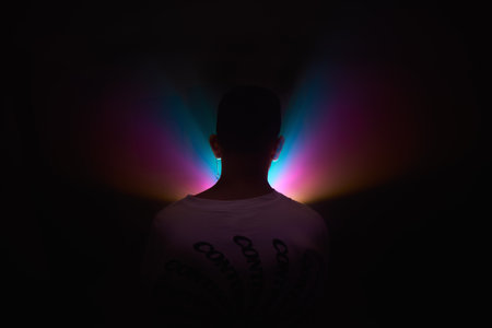 A close up shot on the back of a young guy looking to a colorful lights inside a dark placeの写真素材