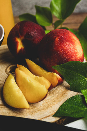 A vertical shot of peaches whole and sliced on a wooden surface, surrounded by leavesの写真素材