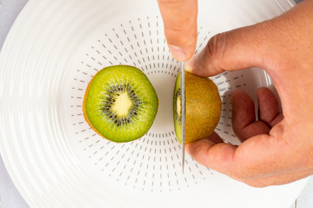 A top view of hands cutting a kiwi on a plate